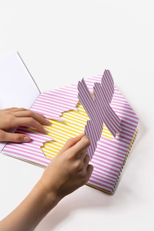 hands detach pink paper cabin from book