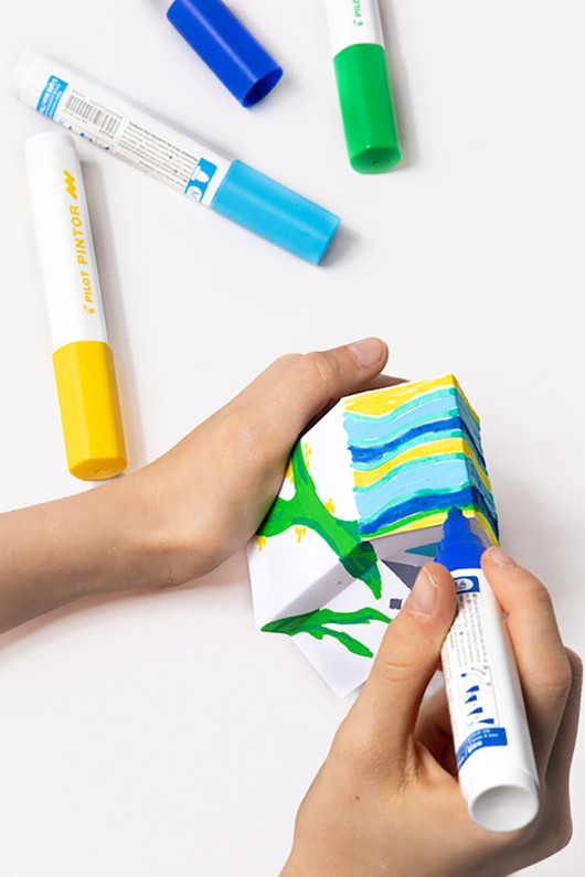 hands-color-paper-cabin-with-blue-yellow-and-green-markers